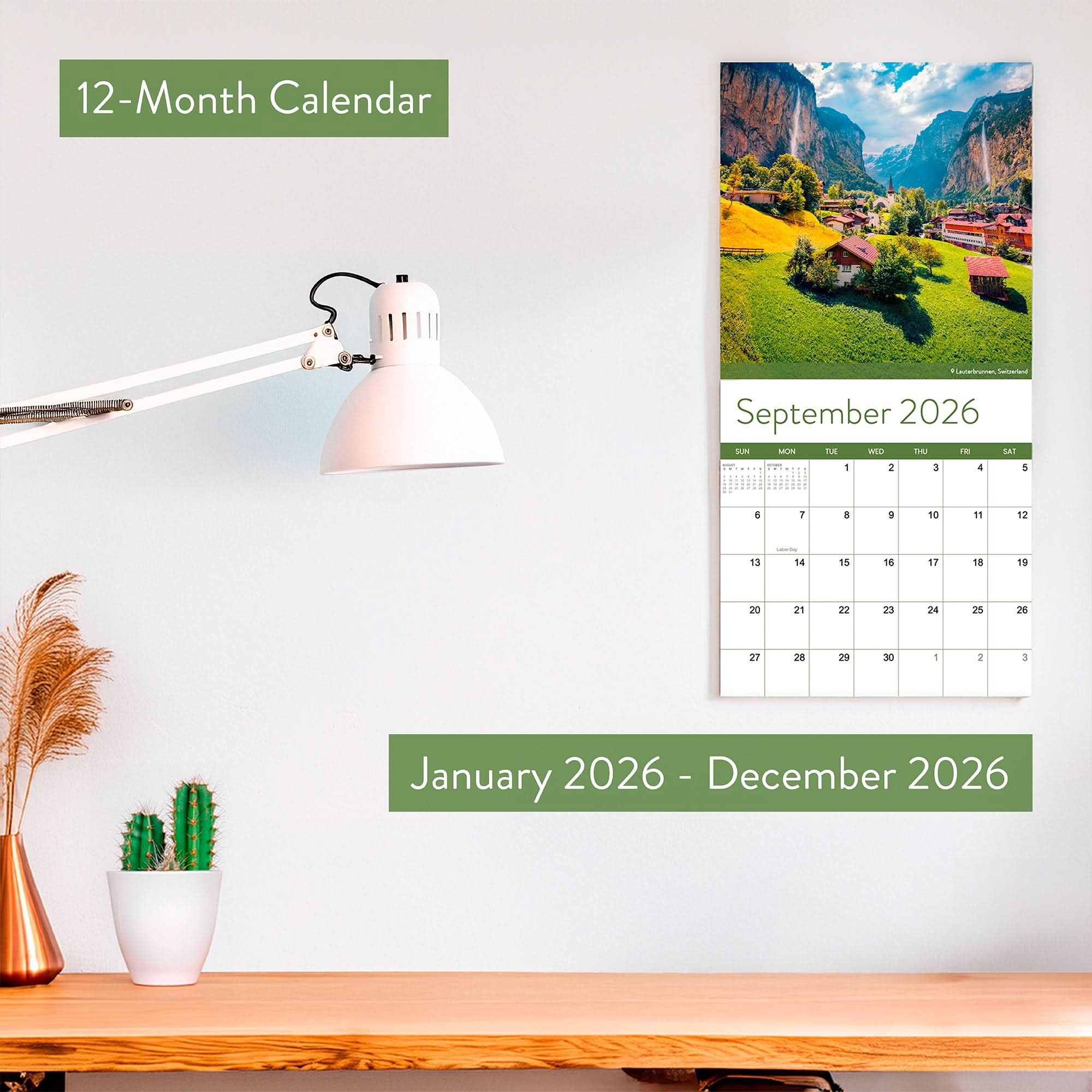 The Eterna Goods 2026 Travel Inspiration Wall Calendar, with stunning coastal photography and January–December 2026 coverage, hangs above a desk decorated with a lamp, small plant, and cactus opened to September.