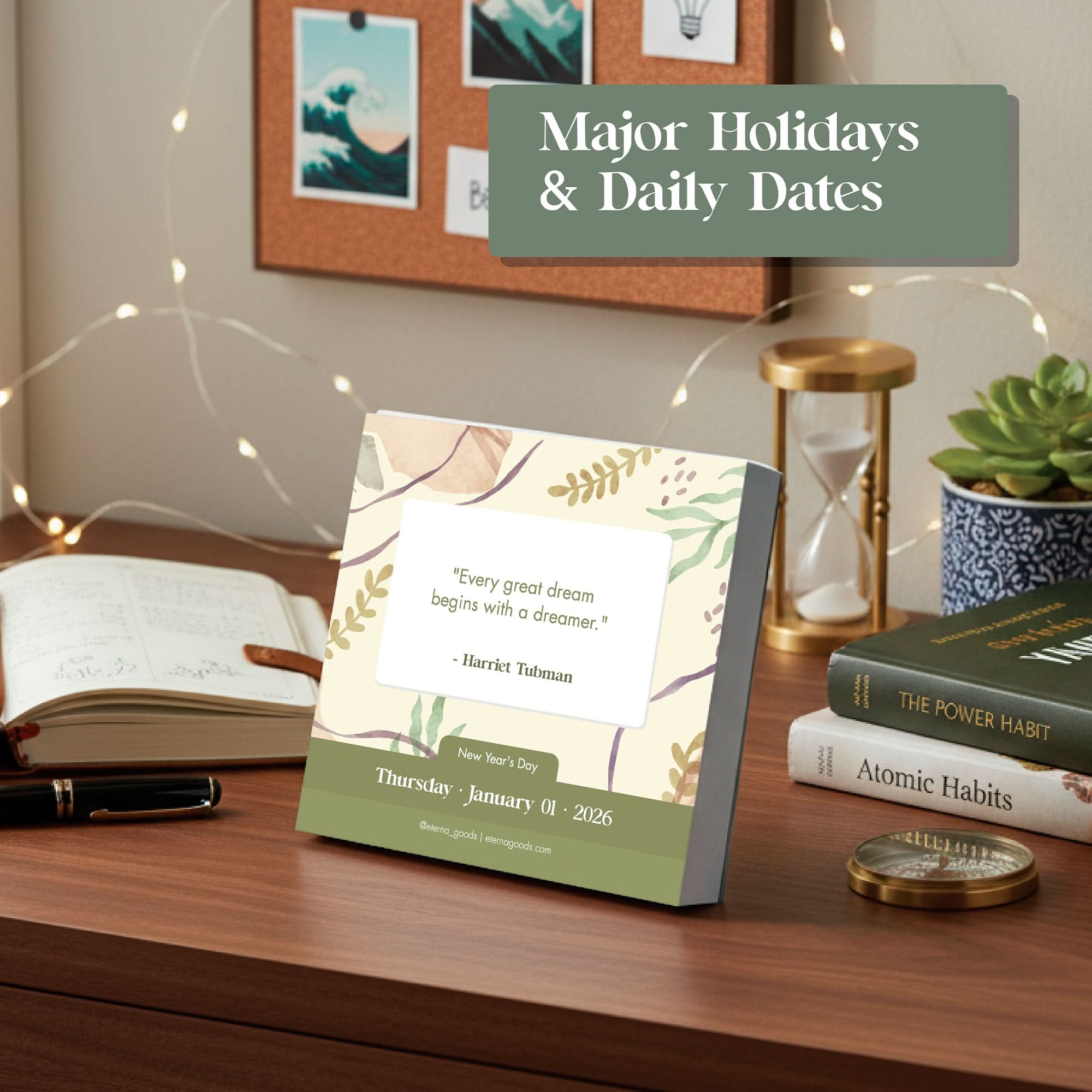On a desk sits Eterna Goods’ 2026 Motivational Calendar showing January 1 with a Harriet Tubman quote, alongside an open notebook, pen, plant, candle, and books—including "Atomic Habits.
