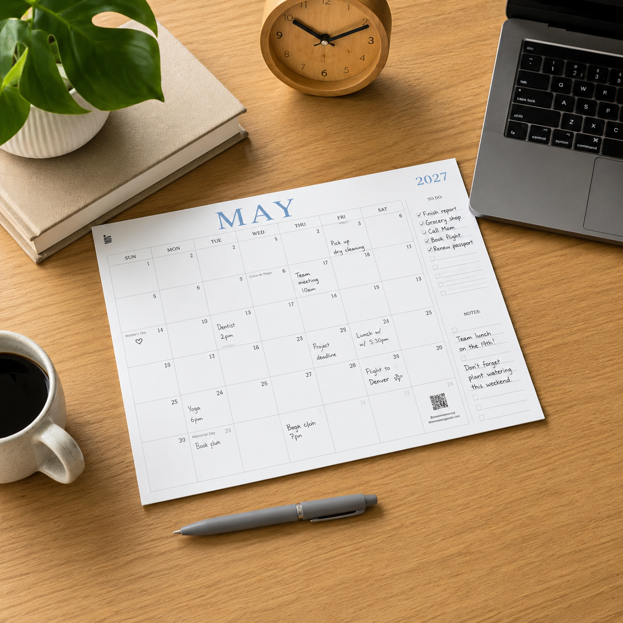 A blank August 2026 wall calendar hangs on a gray concrete wall above a white table and wooden chairs, with a small green plant in the foreground.