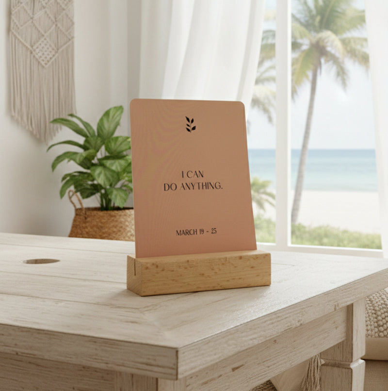 A card in a wooden holder displays the text "I CAN DO HARD THINGS. JAMES 1:17" with a small leaf graphic above the text, set against a plain background.