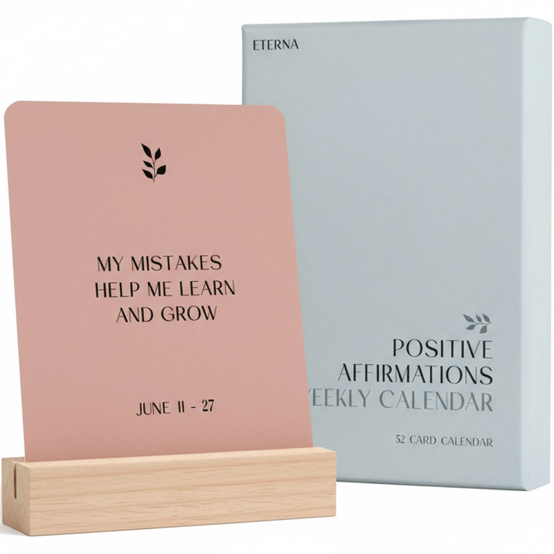 A pink “My mistakes help me learn and grow” card (June 11–27) from the Eterna Goods Positive Affirmation Cards Weekly Calendar sits in a wooden holder beside its light blue box—an ideal self-care and mindfulness gift.
