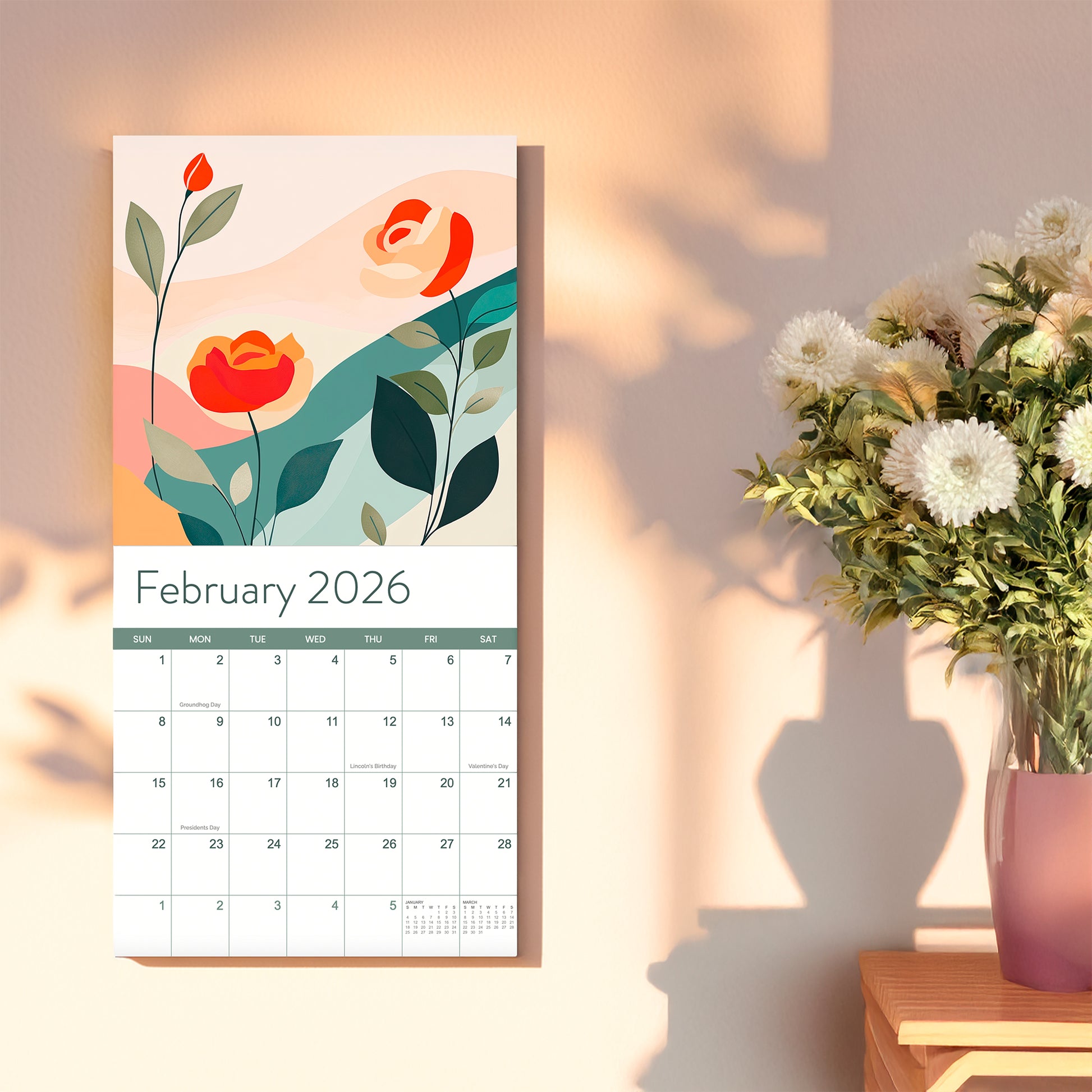 The 2026 Floral Wall Calendar by Eterna Goods is open to February, displaying an abstract floral design beside a vase of white flowers on a sunlit table.