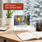 A desk with the Hannah Faith 2026 Verse A Day Calendar showing mindful verses, a plant, a cup, and an open notebook; outside the window, snow-covered trees are visible.