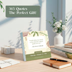 A desk featuring the Eterna Goods 2026 Motivational Calendar displaying a quote, surrounded by white flowers in a vase, books, a pen, and gift boxes.