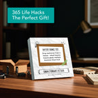 The Eterna Goods 2026 Daily Life Hacks Calendar sits on a desk with batteries and books, displaying a tip about testing batteries by bouncing them—a practical gift for any workspace.