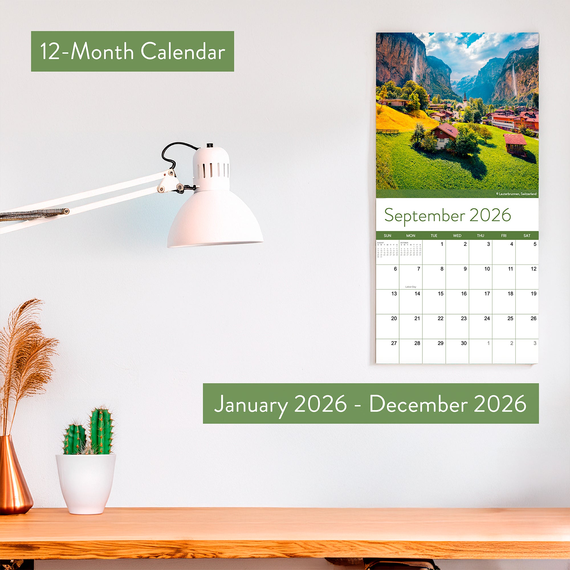 The Eterna Goods 2026 Travel Inspiration Wall Calendar, with stunning coastal photography and January–December 2026 coverage, hangs above a desk decorated with a lamp, small plant, and cactus opened to September.