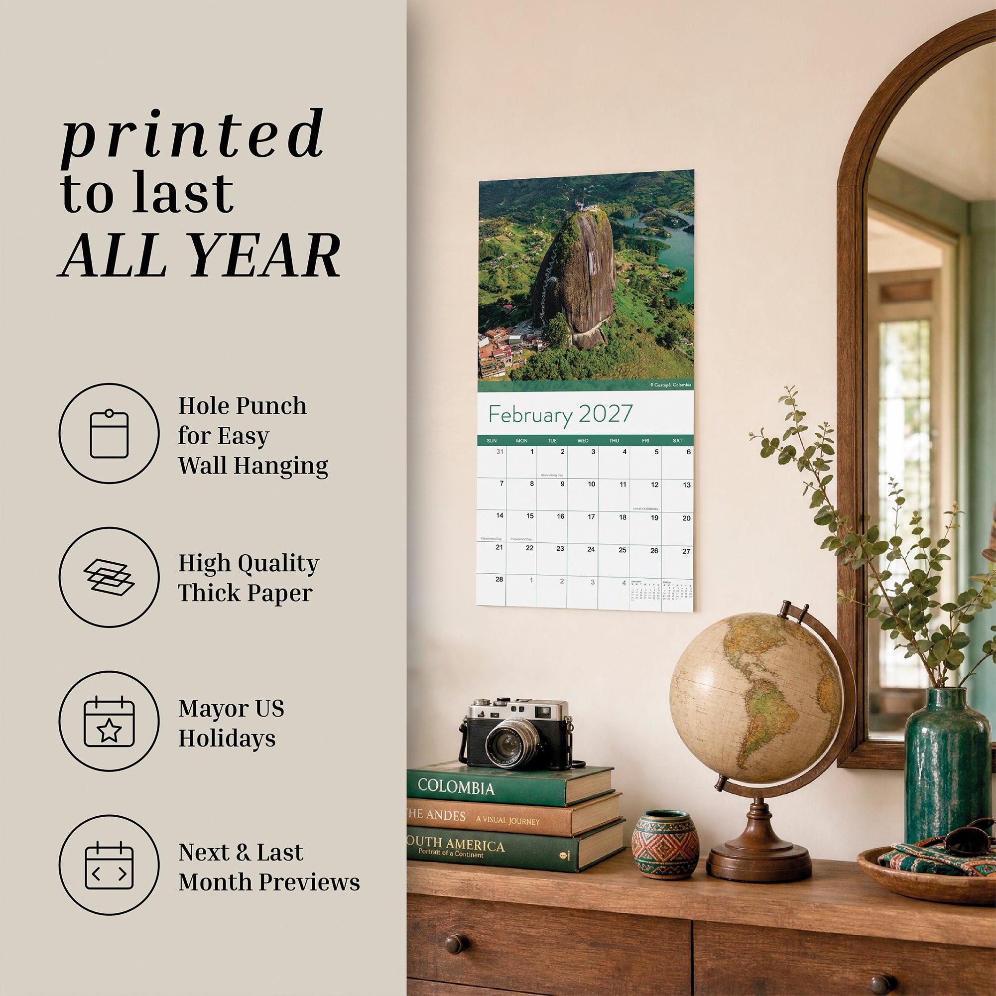 An Eterna Goods 2027 Travel Inspiration Wall Calendar hangs above a dresser adorned with books, a camera, a globe, and lush plants. Text on the image highlights the calendar’s standout features—including thick paper, marked US holidays, and handy monthly previews—making it perfect for sparking your wanderlust all year long.