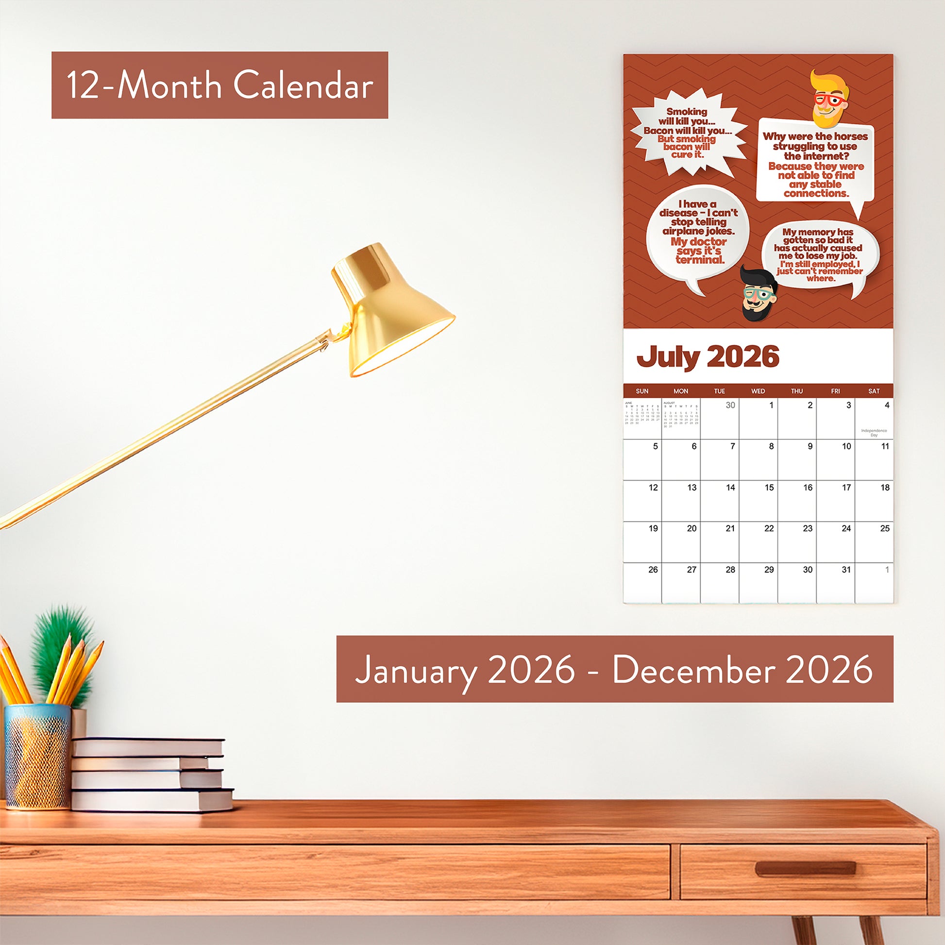 A modern desk setup with a gold lamp, books, and a pencil holder beside a wall-mounted 2026 Dad Joke Wall Calendar by That Is So Dad, open to July and featuring comics and bold text.