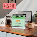 The rockdoodles A Pun A Day Perpetual Calendar, open to February 12, is displayed with coffee mugs, a French press, and a burlap bag on a wooden desk. "USE IT YEAR AFTER YEAR!"—a fun wordplay gift for coffee lovers.