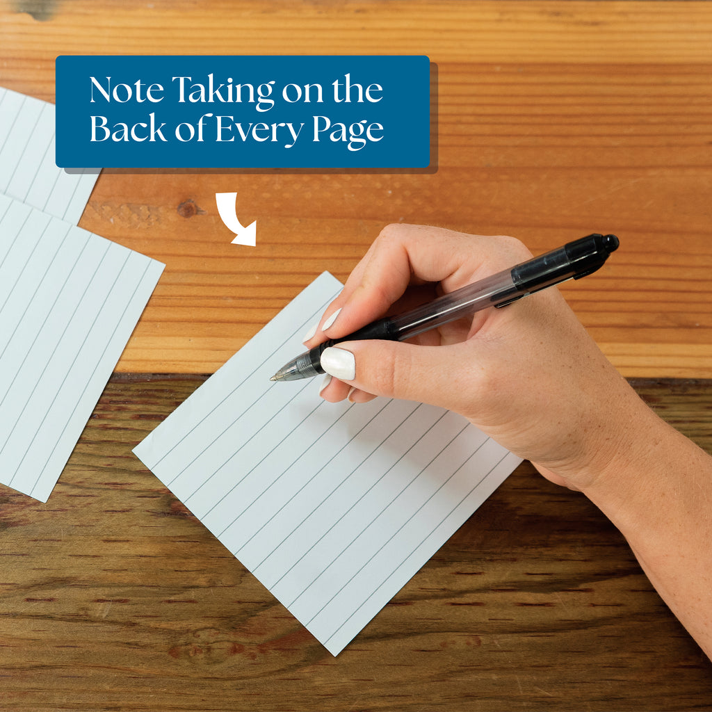 A hand writes with a black pen on a lined note card, beneath the text “Note Taking on the Back of Every Page”—perfect for capturing thoughts sparked by your Eterna Goods 2026 Daily Affirmations Calendar.