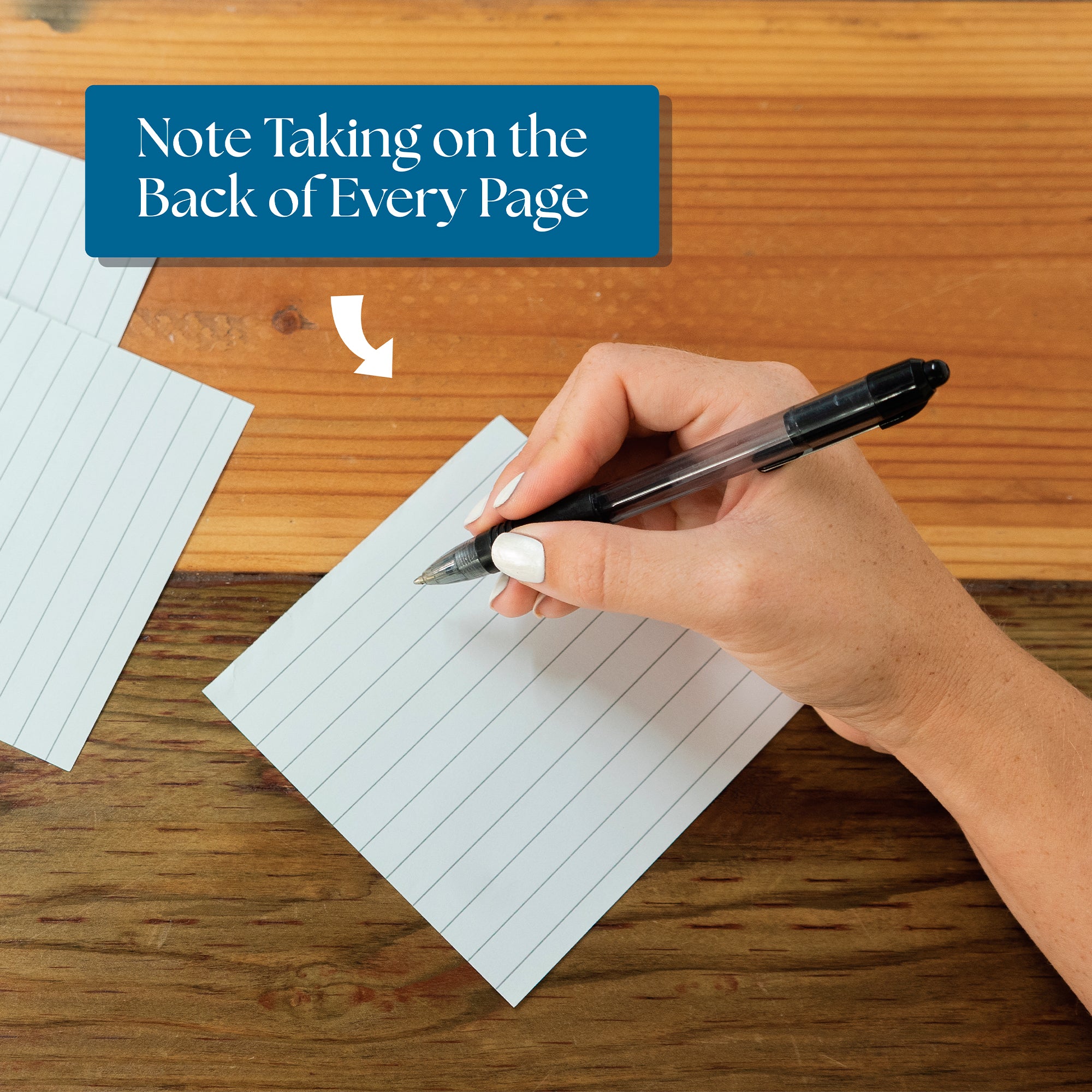 A hand writes with a black pen on a lined note card, beneath the text “Note Taking on the Back of Every Page”—perfect for capturing thoughts sparked by your Eterna Goods 2026 Daily Affirmations Calendar.