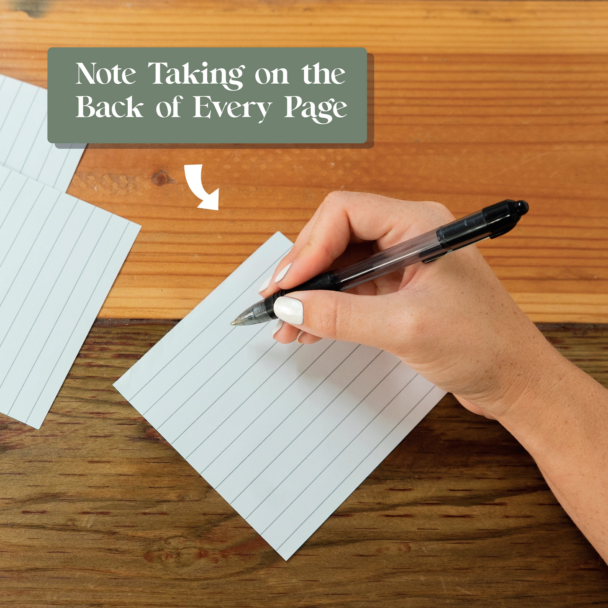 A hand holding a pen writes on the back of a lined note card; above, it reads, "Note Taking on the Back of Every Page"—ideal for jotting daily inspiration or reminders with your 2026 Motivational Calendar by Eterna Goods.
