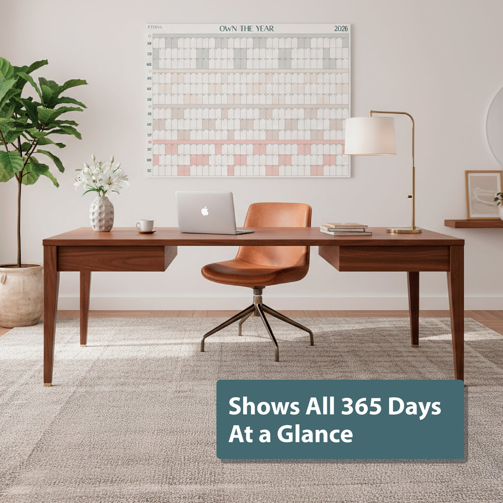 Modern home office featuring Eterna Goods' Own the Year 2026 GIANT Dry Erase Wall Calendar (4ft x 3ft full year planner) above a wooden desk, tan chair, lamp, and plant; sign says, "Shows All 365 Days At a Glance.