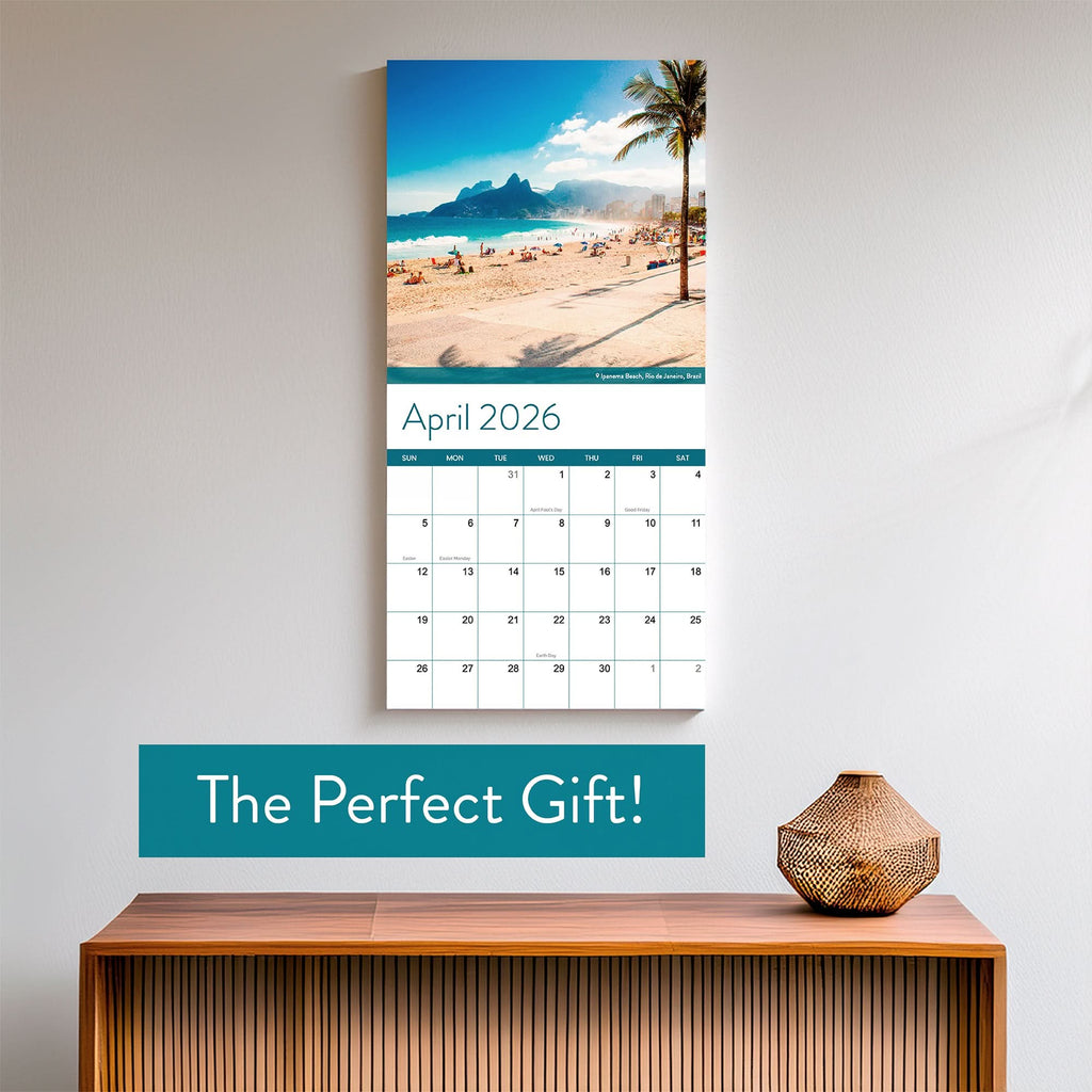 The Eterna Goods 2026 Beaches Wall Calendar shows April with a stunning coastal beach photo and "The Perfect Gift!" below, displayed above a wooden table with a decorative vase.
