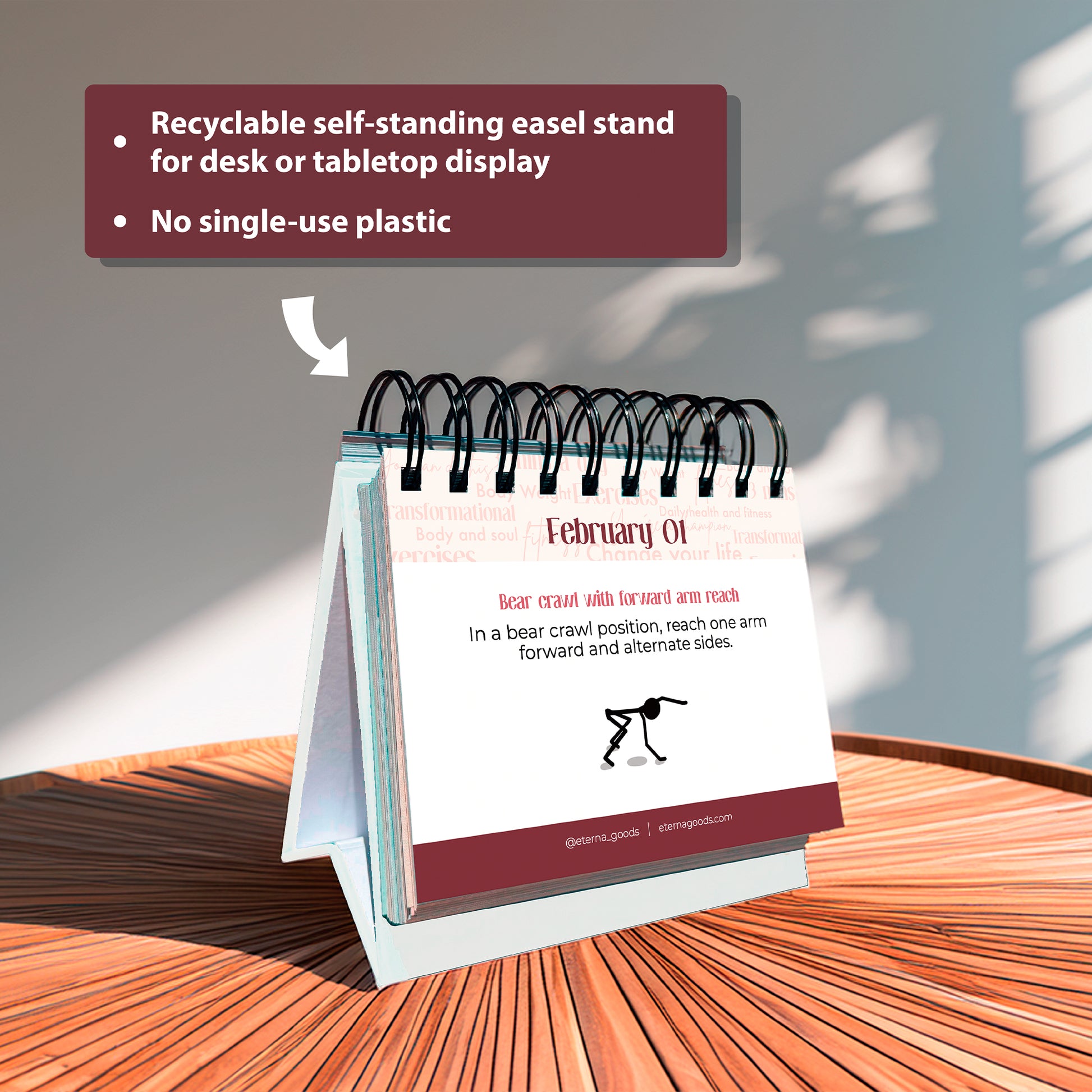 The Eterna Goods Perpetual Fitness Calendar stands on a wood surface, open to an exercise for February 1. Sunlight casts shadows, highlighting that it's recyclable and made without single-use plastic.