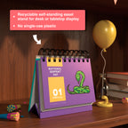 A Holiday Everyday Perpetual Calendar by Eterna Goods, open to February 1st for "National Serpent Day" with a snake illustration, sits on a wooden shelf with party items—perfect for tracking unique holidays year-round.