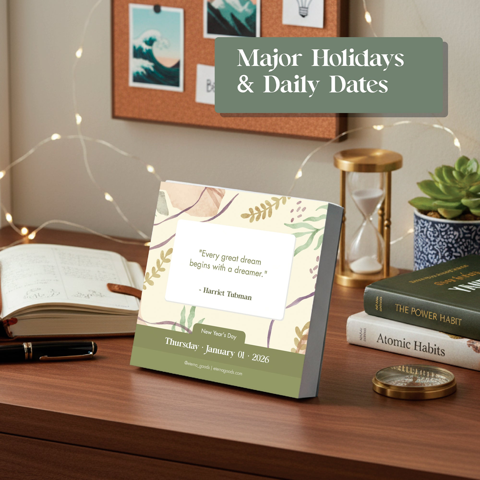 On a desk sits Eterna Goods’ 2026 Motivational Calendar showing January 1 with a Harriet Tubman quote, alongside an open notebook, pen, plant, candle, and books—including "Atomic Habits.