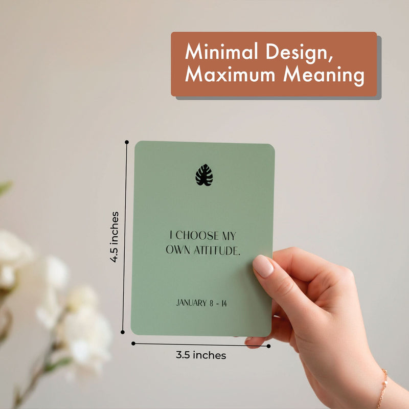 A hand holds an Eterna Goods 3.5 x 4.5 inch Positive Affirmation Card reading "I CHOOSE MY OWN ATTITUDE. JANUARY 8 - 14." Caption: "Minimal Design, Maximum Meaning"—the perfect mindfulness gift from the Weekly Calendar set.