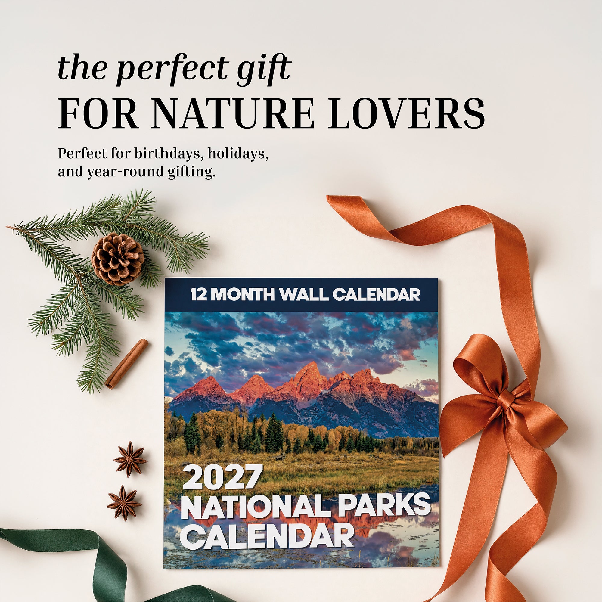 The 2027 National Parks Wall Calendar by Eterna Goods is beautifully displayed with ribbon, pinecone, and evergreen branch on a light surface—making it the perfect gift for outdoor enthusiasts who admire breathtaking National Park photography.