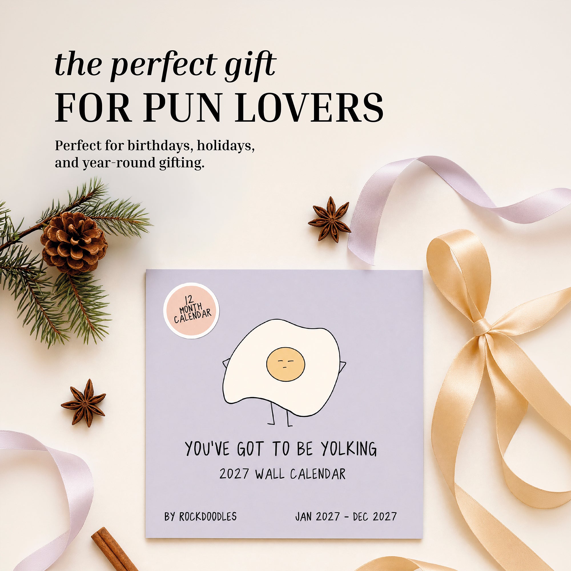 The 2027 Pun Wall Calendar by rockdoodles, featuring a cartoon egg on the cover, is displayed alongside pinecones, ribbon, and a gift bow—highlighting it as a hilarious calendar and an ideal present for fans of puns.