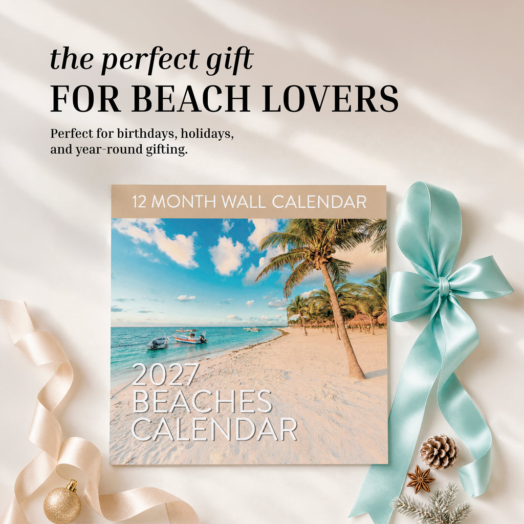 The 2027 Beaches Wall Calendar by Eterna Goods is displayed on a beige surface with a blue ribbon and gold ornament, alongside text inviting beach lovers to enjoy it as the perfect gift. Showcasing stunning beach photography, this 12-month calendar lets you experience breathtaking shores all year long.
