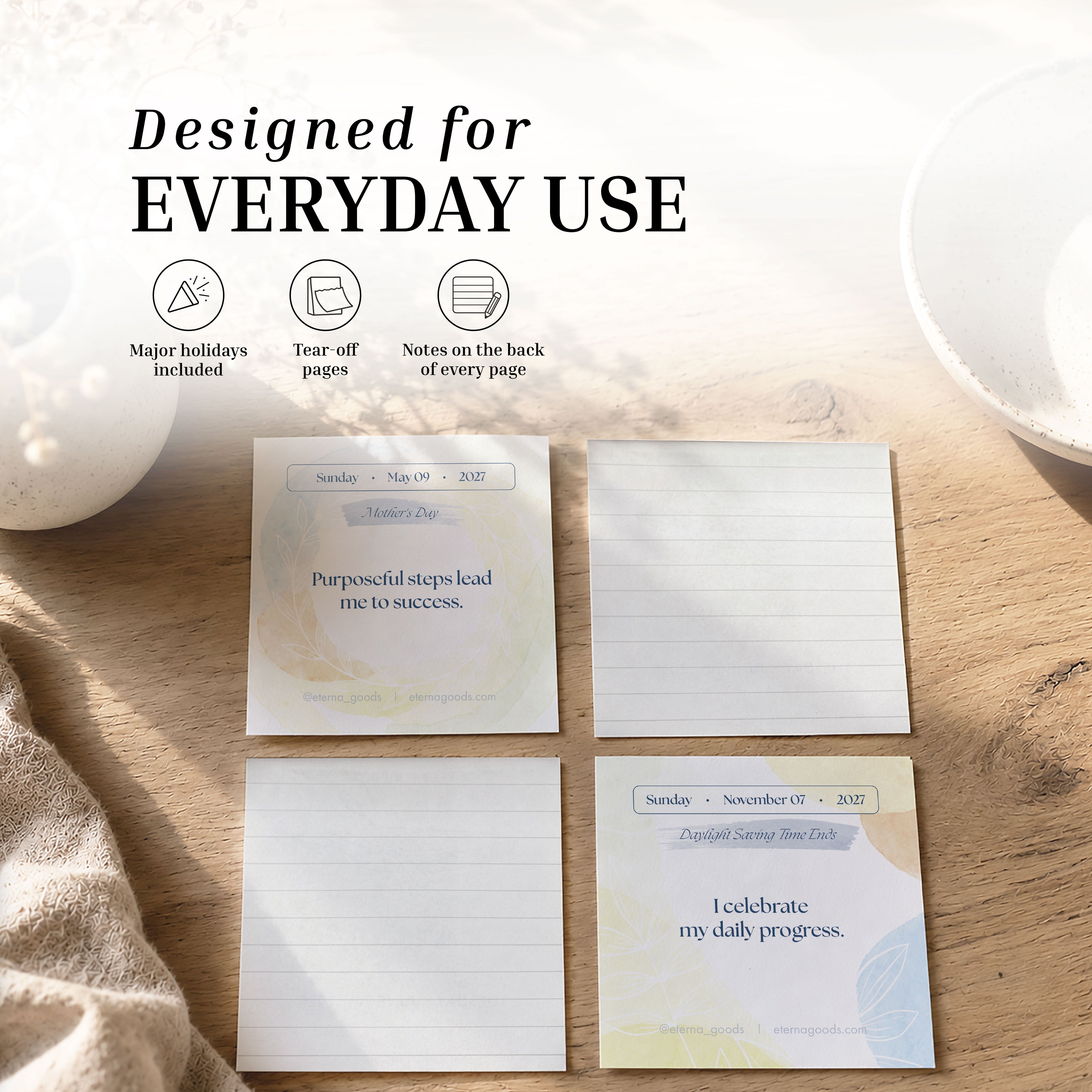 The Eterna Goods 2027 Daily Affirmations Calendar is shown as four notepads with motivational quotes and tear-off pages arranged on a wooden surface, alongside text showcasing features such as major holidays, space for notes, and suitability for daily use—making it ideal for adding positive affirmations and mindfulness to your everyday routine.