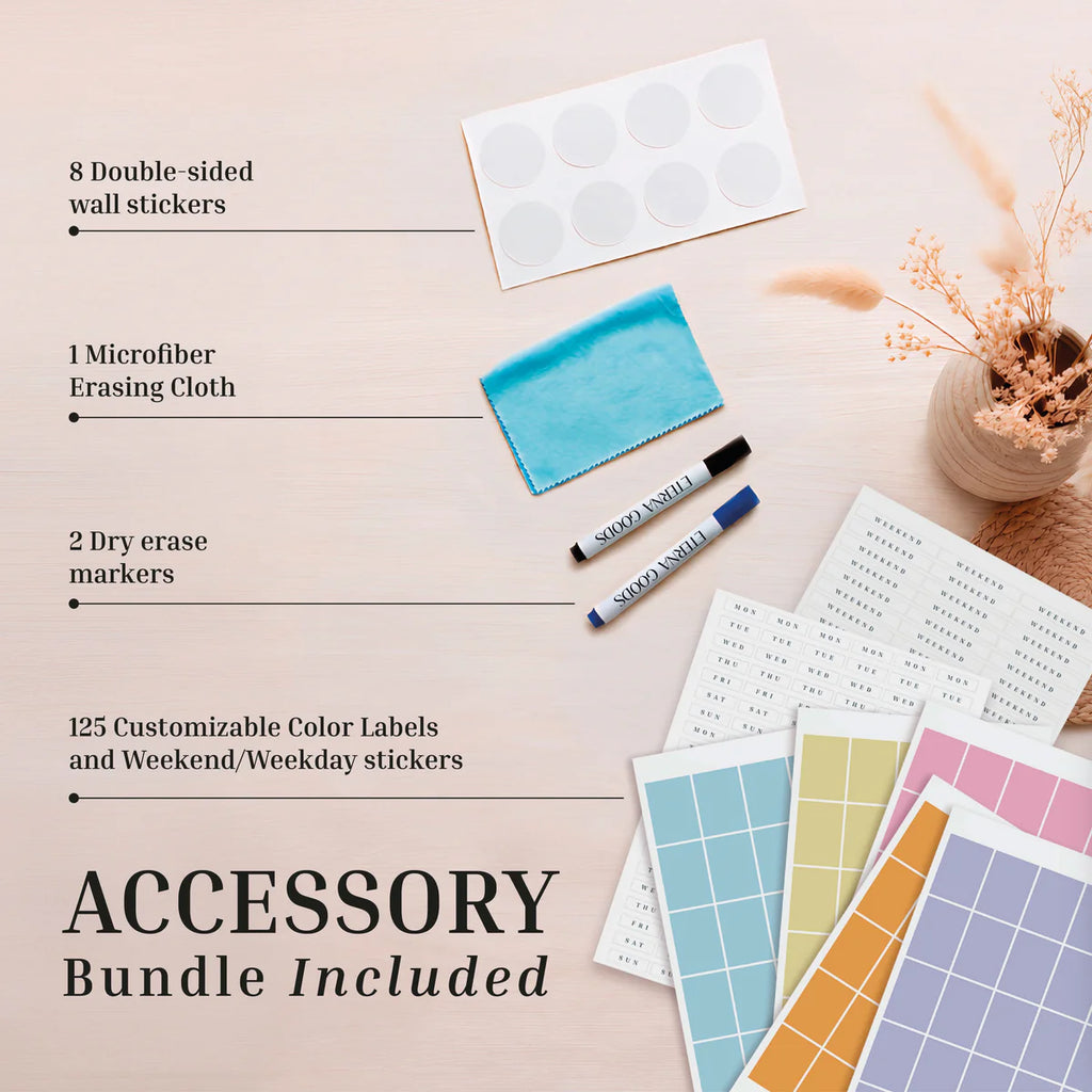 Flat lay of the included accessory bundle for your Eterna Goods Own The Year Giant Dry Erase Calendar: wall stickers, a microfiber cloth, two dry erase markers, 125 color labels, and weekday stickers—all displayed on a light wood surface alongside a decorative vase.