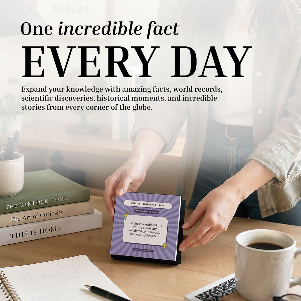 At a desk filled with books, a mug, a pen, and a laptop, someone flips to a new day on the 2027 Epic Facts Calendar by Eterna Goods. A text overlay invites you to discover an incredible fact every day.