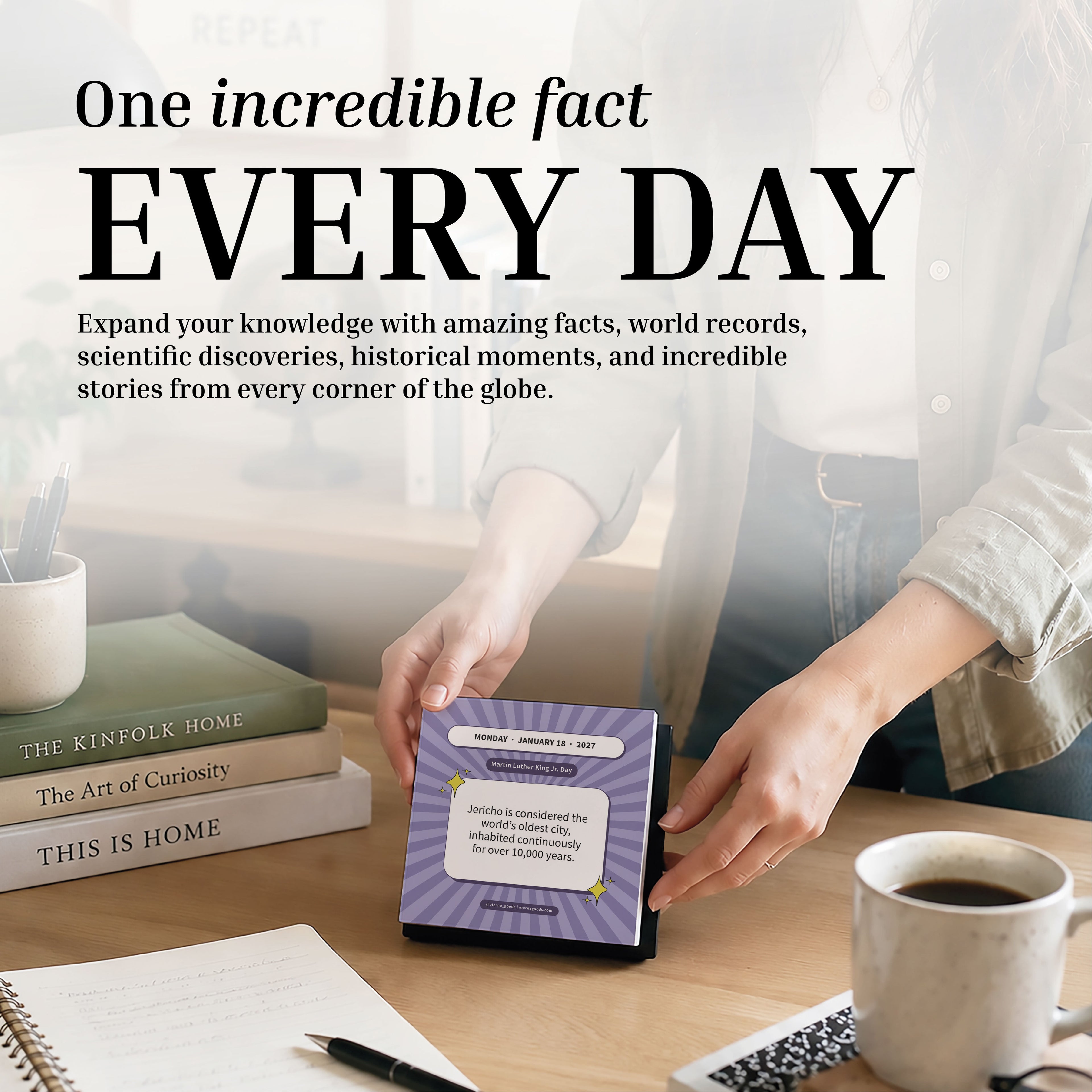 At a desk filled with books, a mug, a pen, and a laptop, someone flips to a new day on the 2027 Epic Facts Calendar by Eterna Goods. A text overlay invites you to discover an incredible fact every day.