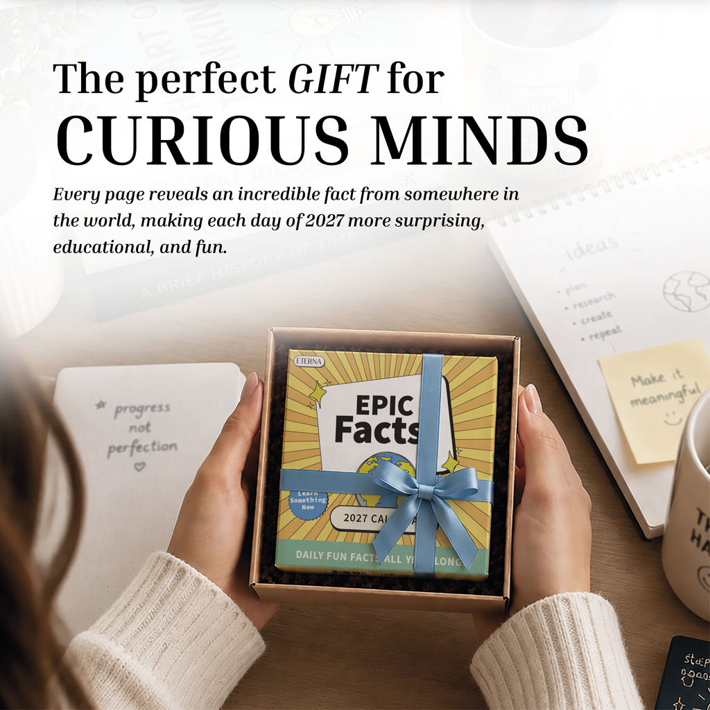 At a desk with notebooks, pens, and paper, someone holds a boxed 2027 Epic Facts Calendar by Eterna Goods, recommending this daily facts calendar as the perfect gift for curious minds.