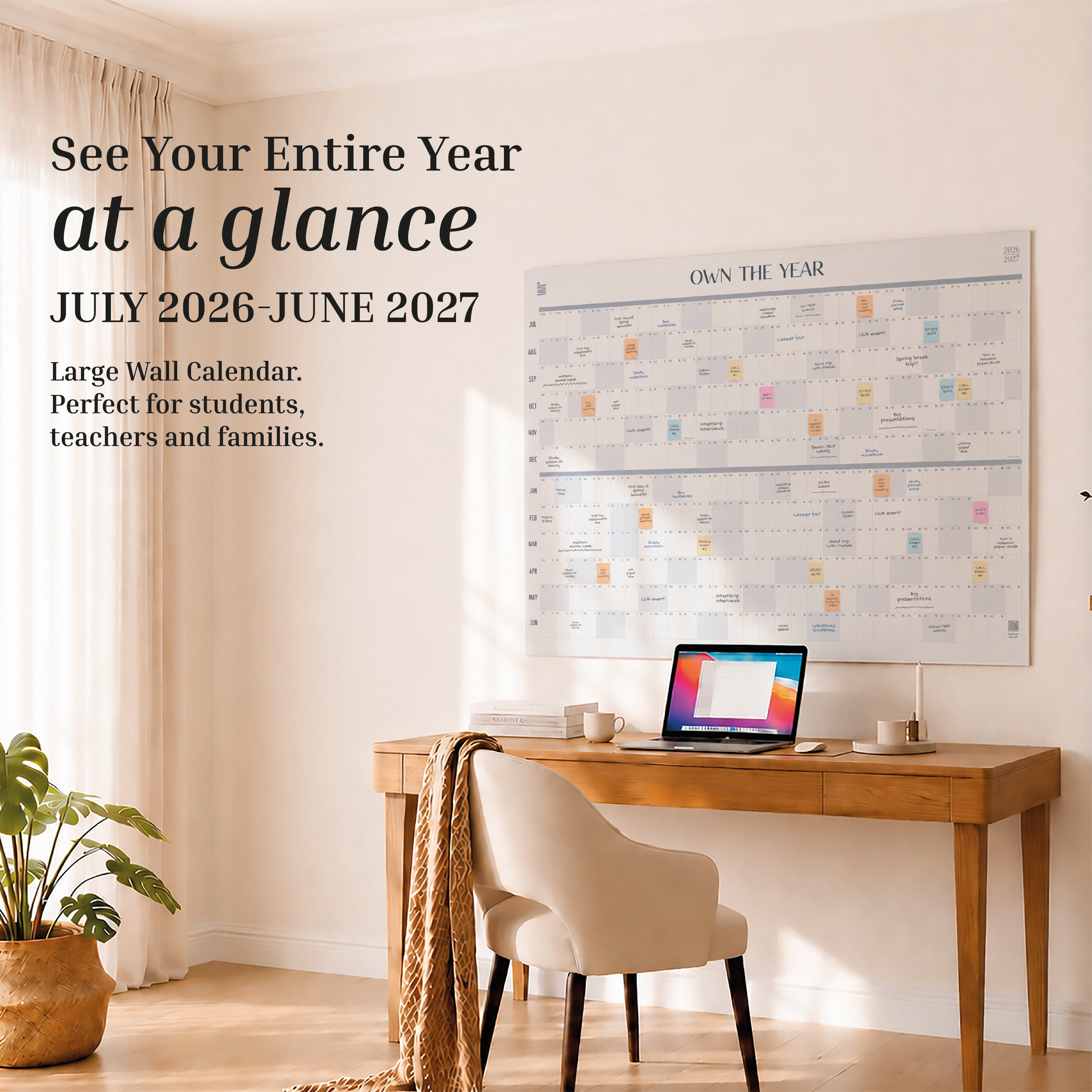 A home office with a desk, chair, laptop, lamp, plant, and an oversized Eterna Goods 2026-2027 Midyear/Academic Own The Year Calendar showing months from July 2026 to June 2027.