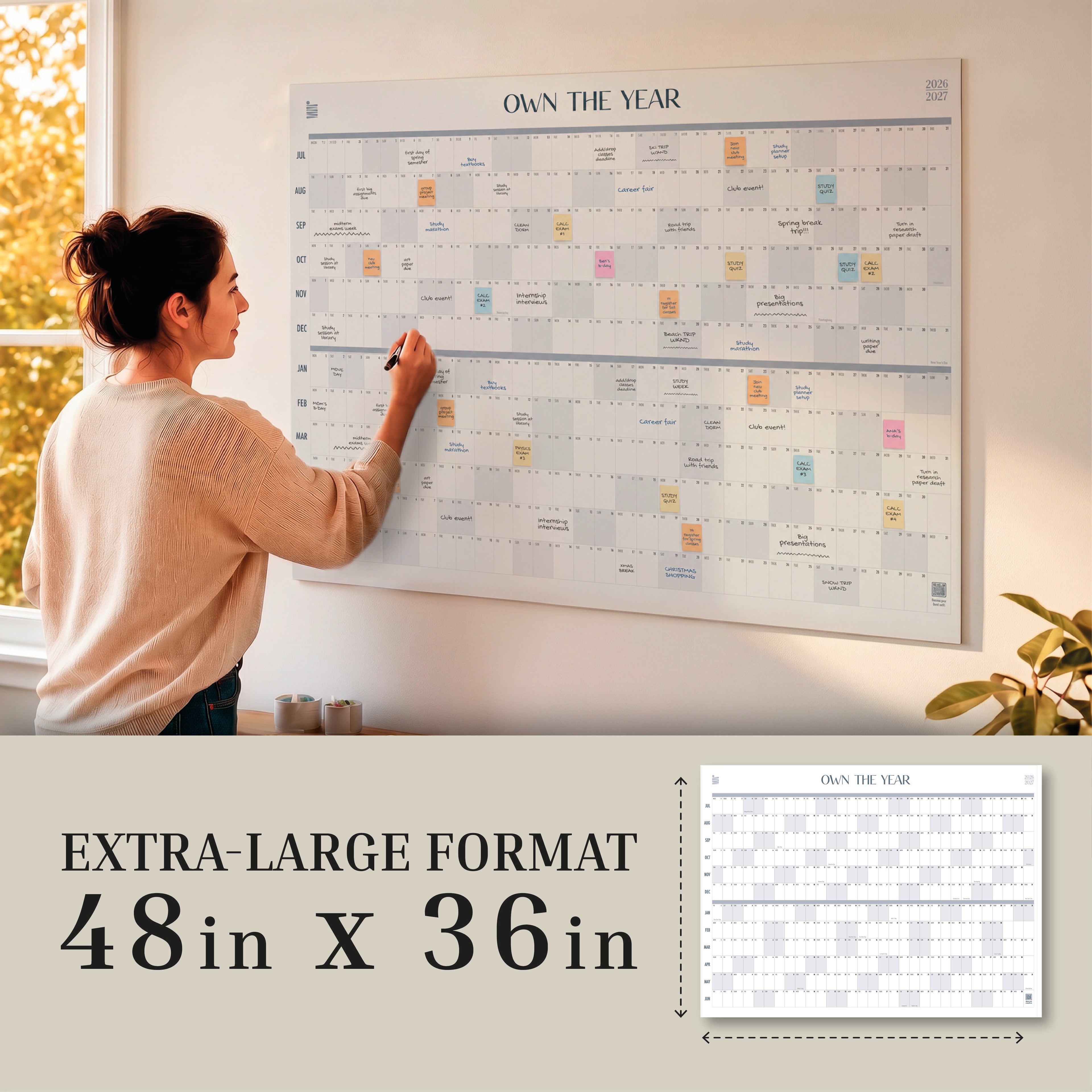 A woman writes on an oversized Eterna Goods 2026-2027 Midyear/Academic Own The Year Calendar in a sunlit room. Text highlights the calendar’s extra-large 48 x 36 inch format.