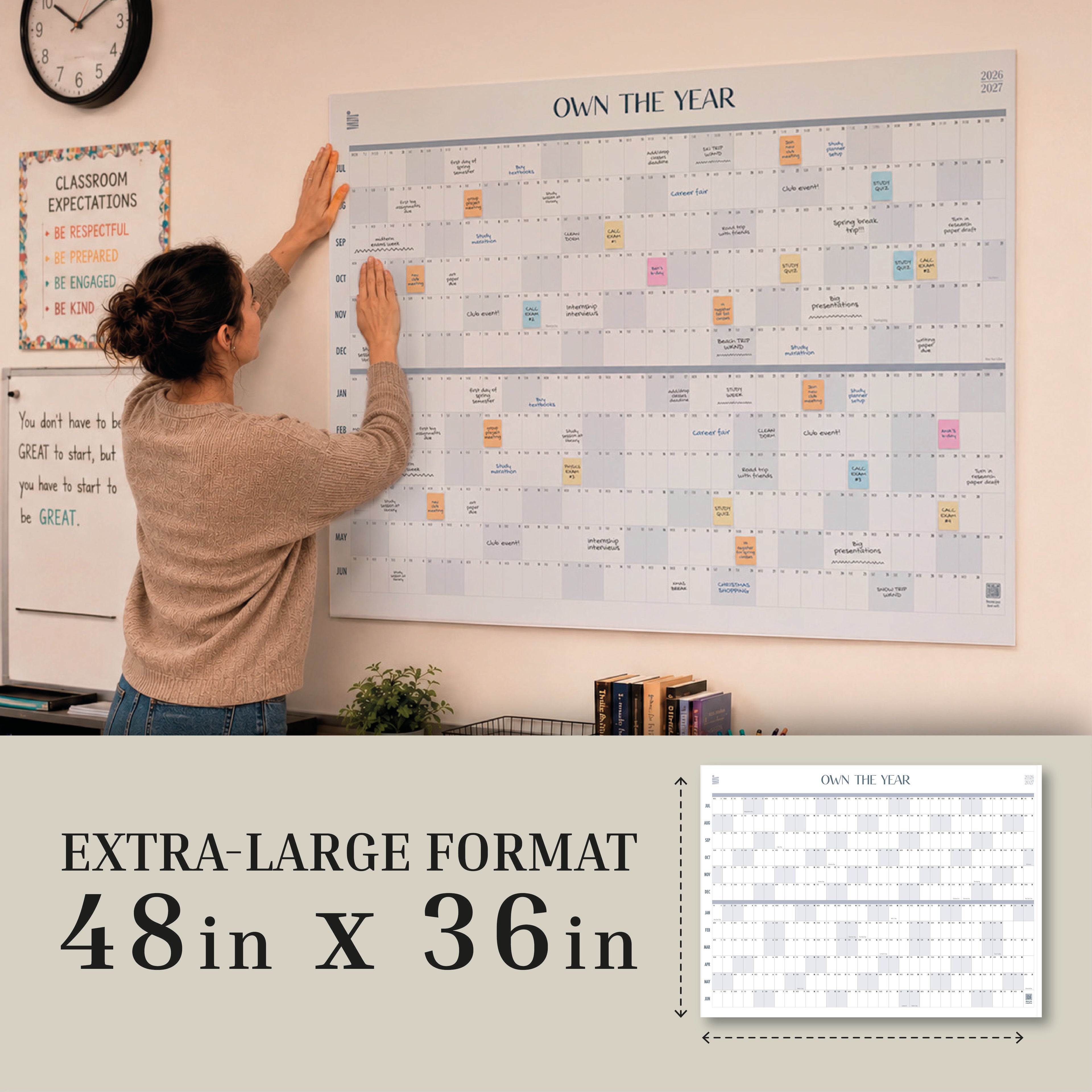 A woman hangs the 2026-2027 Midyear/Academic Own The Year Calendar by Eterna Goods, measuring 48"x36", on a wall above a small shelf.