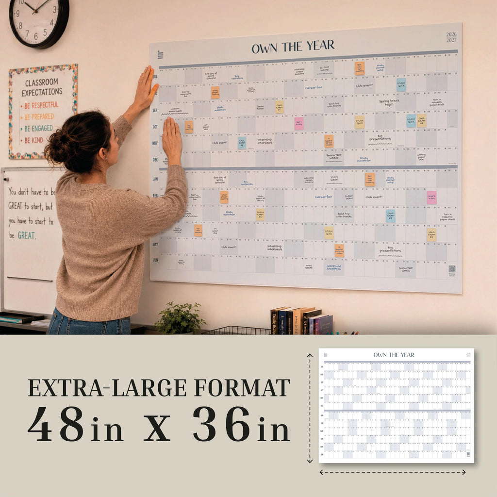 A person mounts an Eterna Goods "Own The Year" Giant Dry Erase Calendar (48 in x 36 in) on the classroom wall, surrounded by motivational posters, allowing everyone to easily track important dates at a glance.