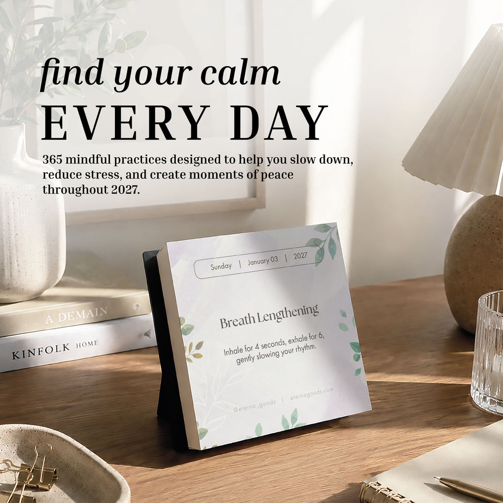 An Eterna Goods 2027 Mindfulness Calendar sits on a wooden table, open to a breathing exercise page, with sunlight and houseplants in the background; text above encourages daily mindfulness exercises and stress relief practices.