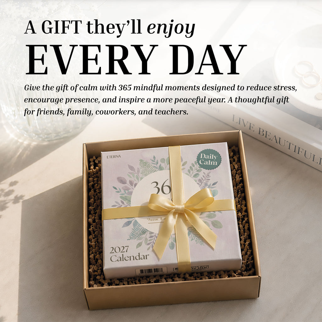 A 2027 Mindfulness Calendar from Eterna Goods, titled "36 Daily Calm," is elegantly wrapped with a yellow ribbon and presented in a gift box, resting on a sunlit table alongside a decorative tray—offering daily mindfulness exercises and stress relief.