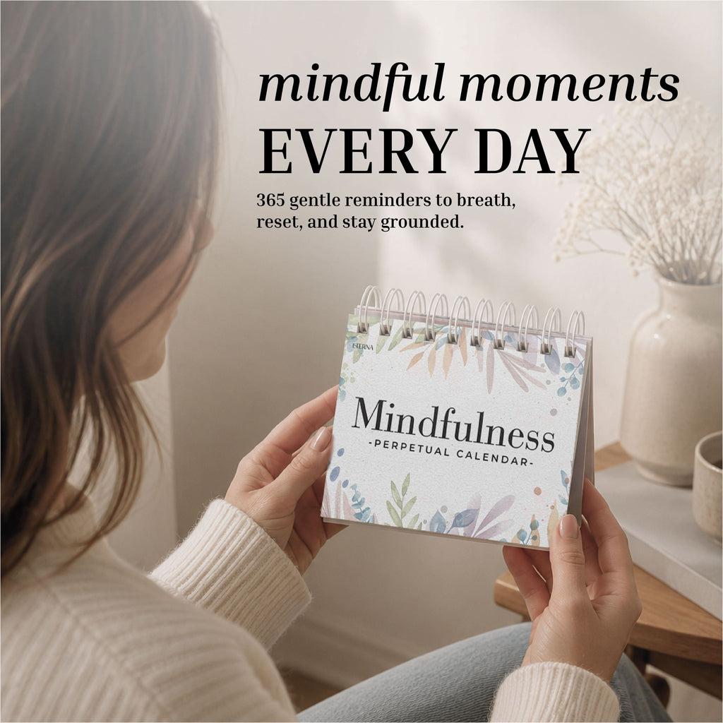 Someone holds an Eterna Goods "Perpetual Mindfulness Calendar" at a table, featuring 365 daily prompts to breathe, reset, and stay grounded.