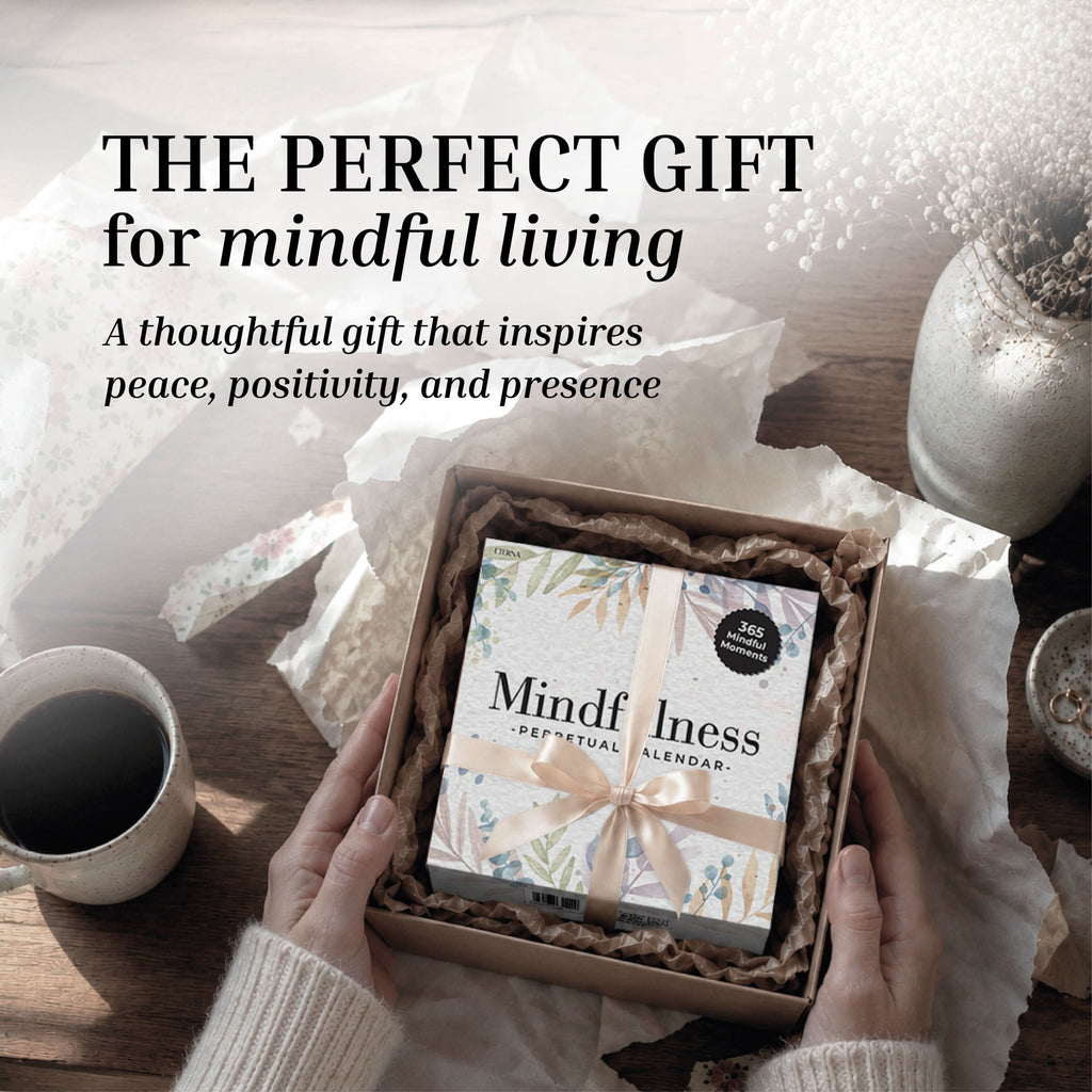 A pair of hands holds an open gift box, revealing the Eterna Goods Perpetual Mindfulness Calendar inside, alongside a cup of coffee and dried flowers on a wooden table. The accompanying text encourages mindful living and thoughtful gifting.