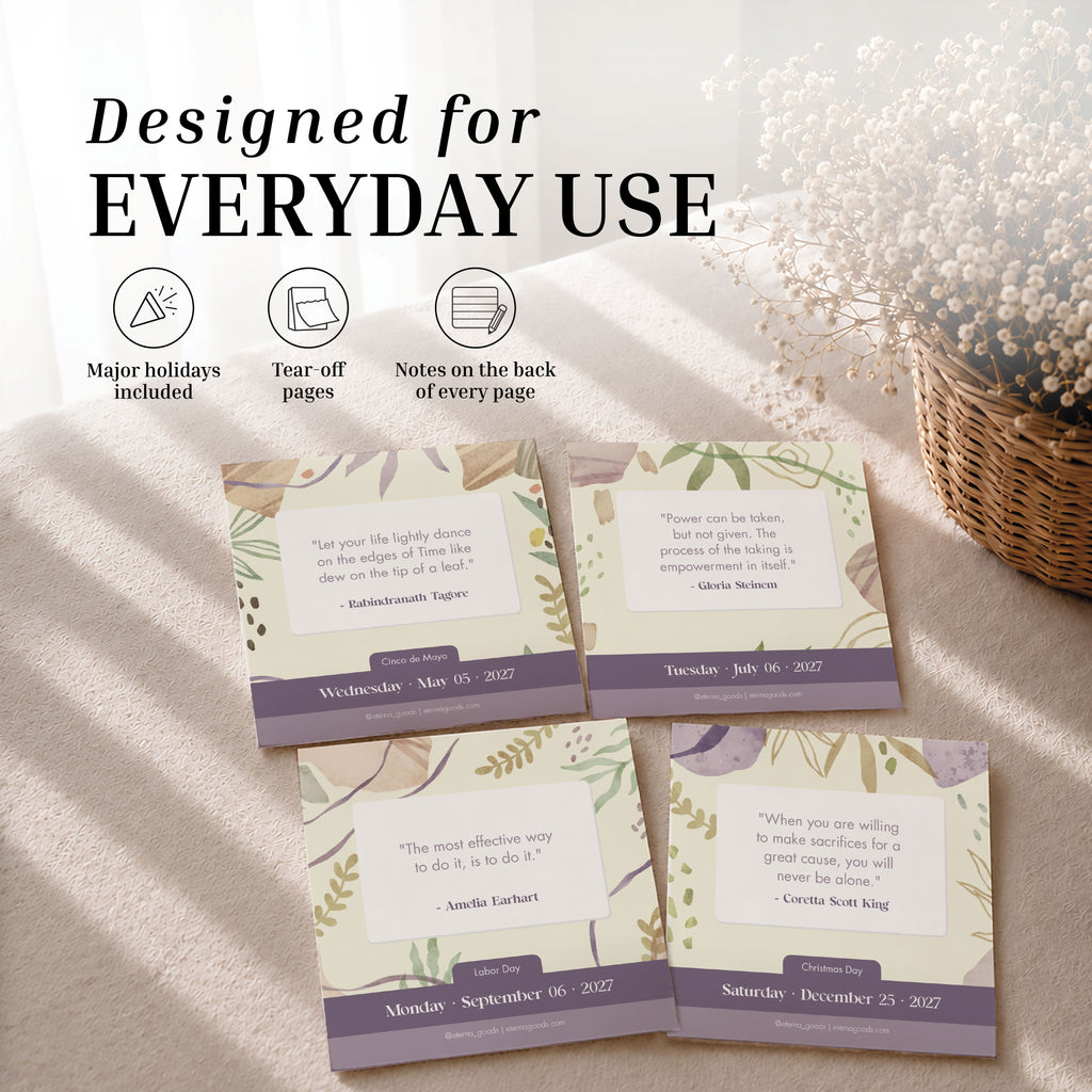 Four pages from the Eterna Goods 2027 Motivational Calendar are arranged on a wooden table beside a vase of dried flowers, with text showcasing features such as major holidays, daily motivational quotes, easy tear-off pages, and space for notes on the back.