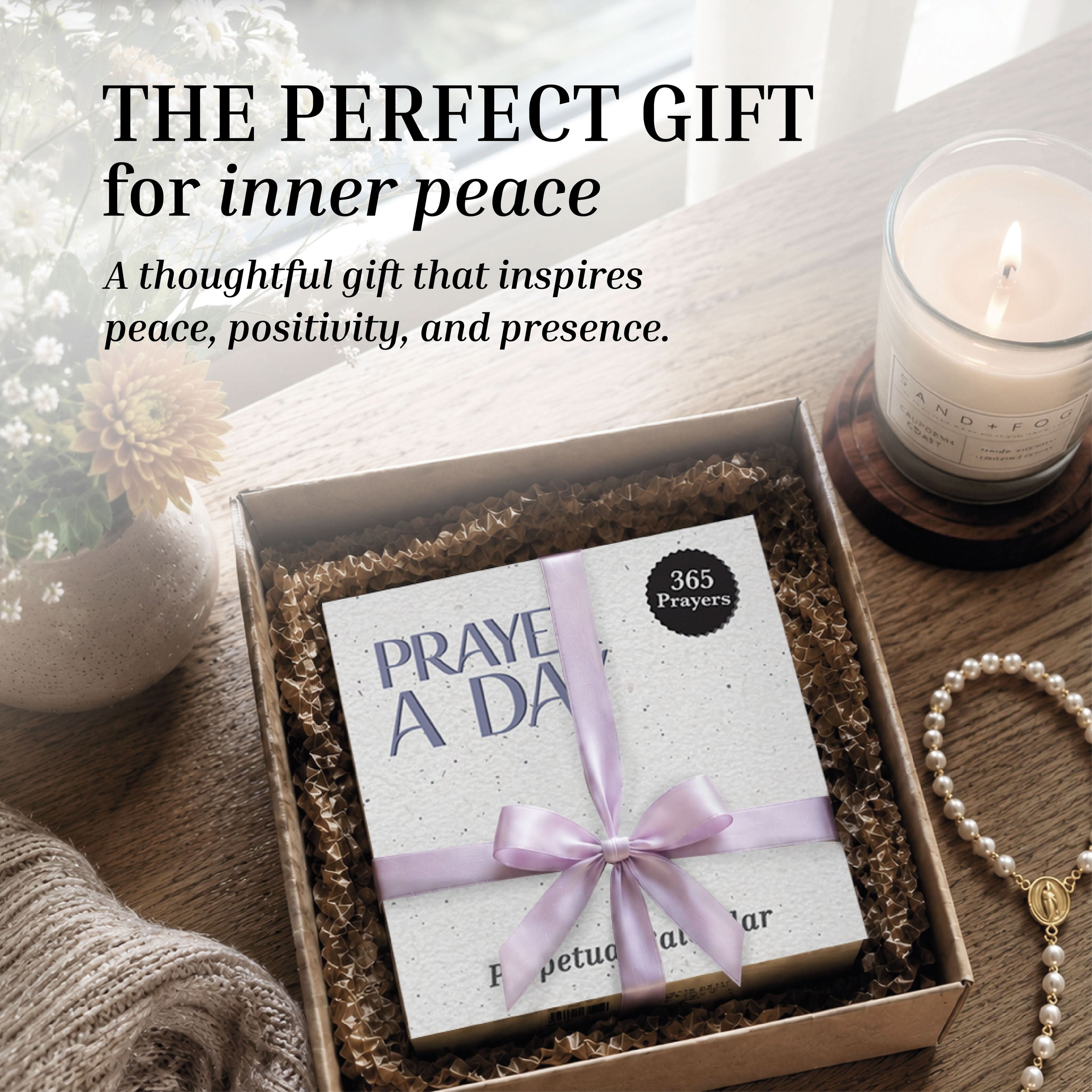 A cozy table arrangement featuring Eterna Goods’ Perpetual Prayer A Day Calendar—beautifully displayed with a lavender ribbon alongside a glowing candle, pen, and bouquet of flowers—invites daily reflection and inspiration, just like having a collection of uplifting prayers always at hand.
