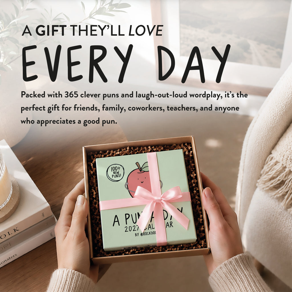 Hands hold an open gift box containing a "2027 A Pun a Day Calendar" by rockdoodles. The box, filled with brown packing material and tied with a pink ribbon, promises endless wordplay and laughter. A cozy, sunlit room is in the background.