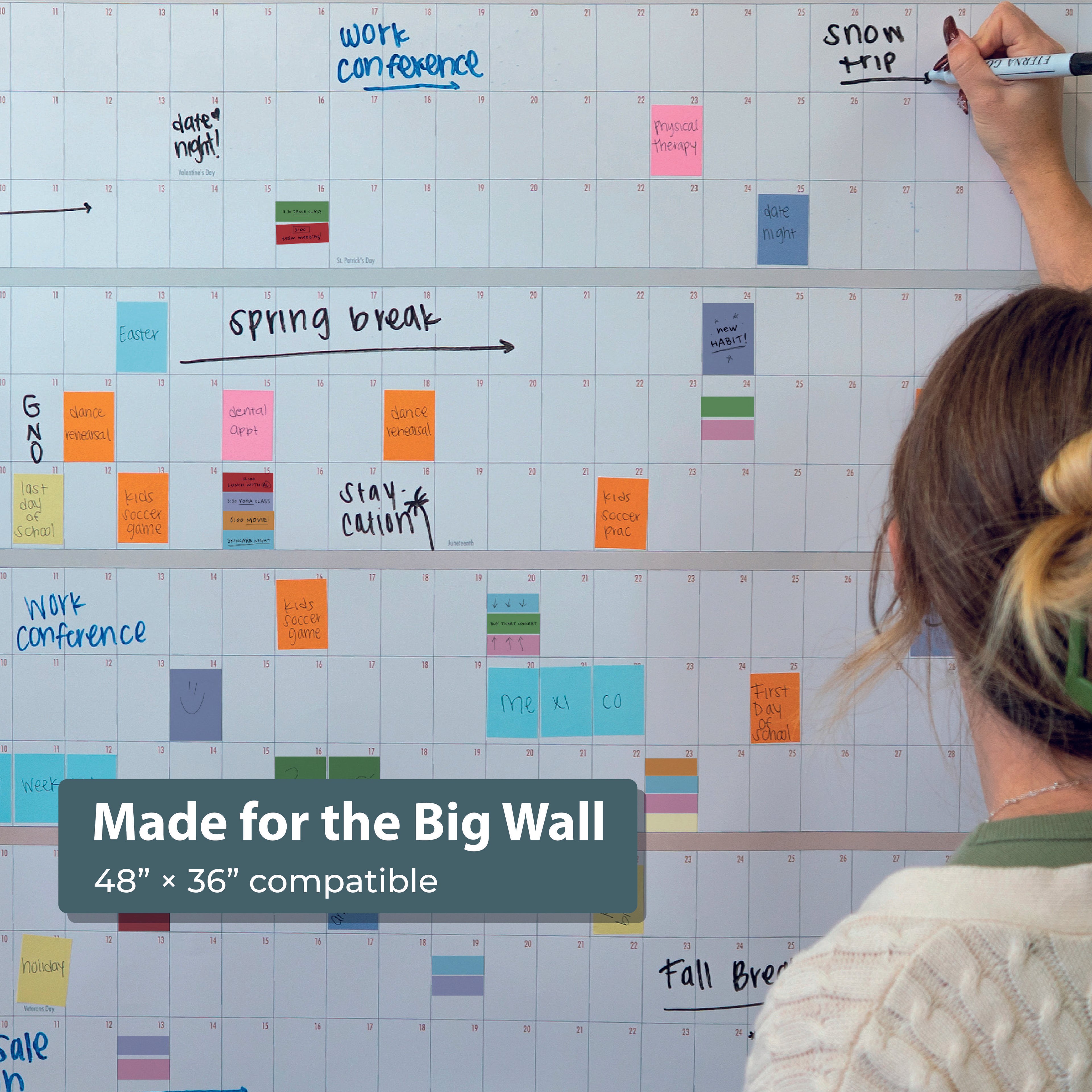 Person writing on a large wall calendar filled with multicolored Planning Block Stickers by Eterna Goods—compatible with 48” x 36” calendars for perfect color-coded planning.