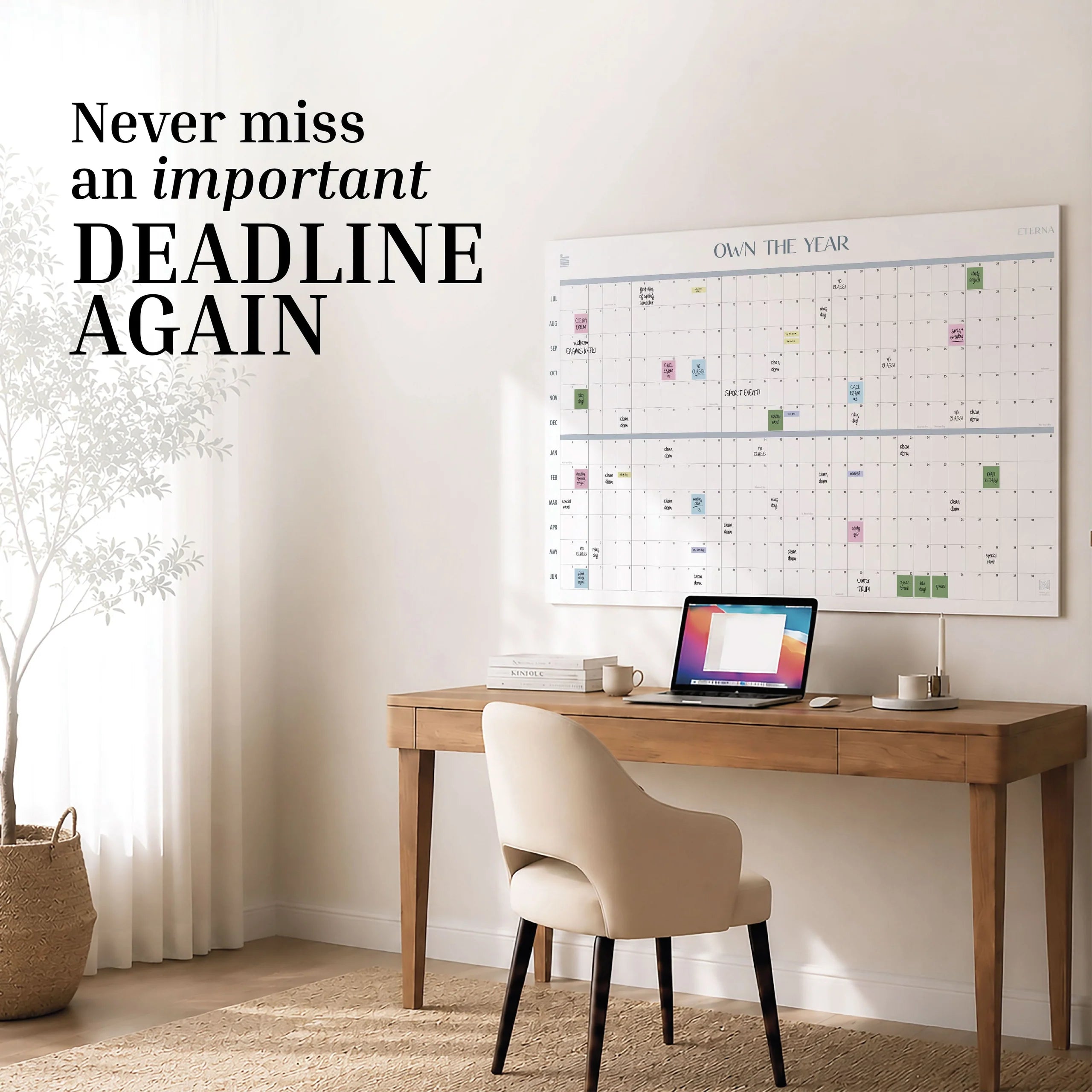 Home office with a wooden desk, chair, laptop, and a giant Own The Year Midyear / Academic Calendar by Eterna Goods on the wall; text reads, “Never miss an important deadline again.”.