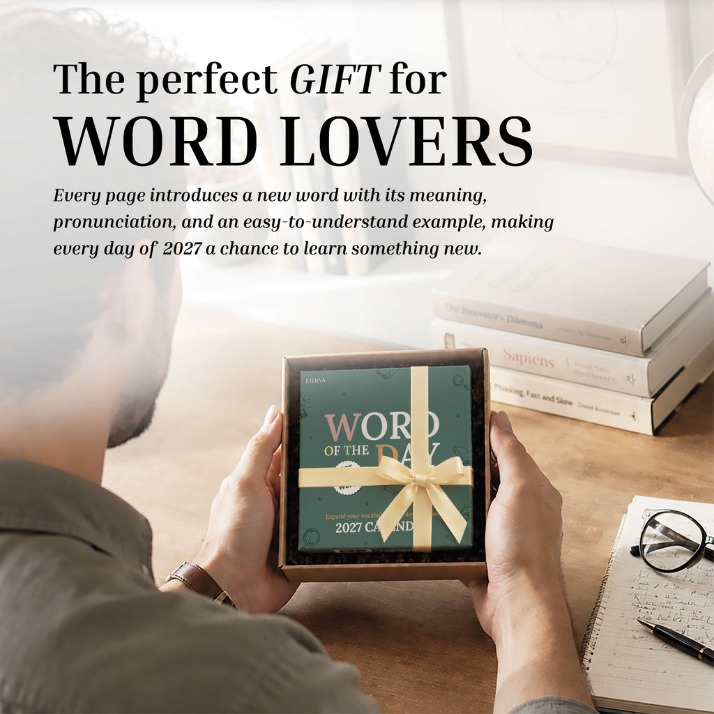 A person sits at a desk with books, glasses, and a coffee cup, holding a ribbon-wrapped Eterna Goods 2027 Word Of The Day Calendar—ready to expand their vocabulary in style.