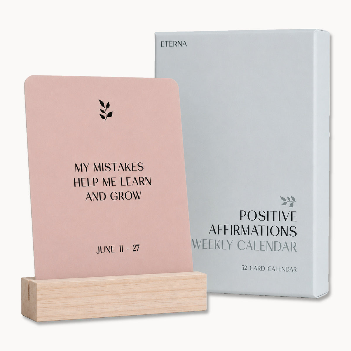 A pink Eterna Goods affirmation card says, "My mistakes help me learn and grow. June 11-27," on a wooden stand beside the Positive Affirmation Cards Weekly Calendar box—a thoughtful self-care gift to inspire daily mindfulness.