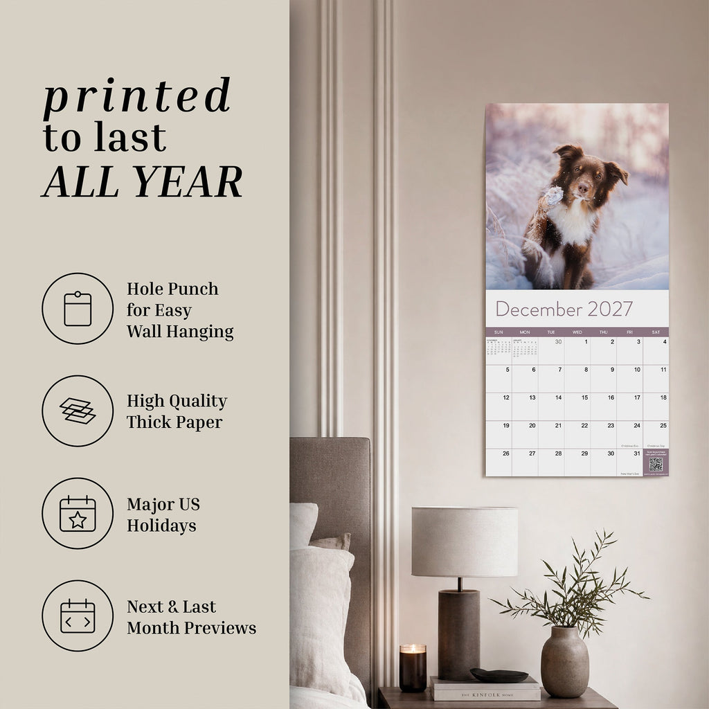 An Eterna Goods 2027 Dogs Wall Calendar, featuring vibrant monthly canine images, hangs above a bedroom desk. Ideal for dog lovers, this calendar highlights key features and details on the left side of the image.